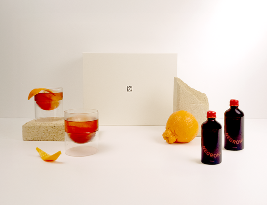 Glass of red liquid with a slice of fruit, lemon, and two bottles on a white surface.