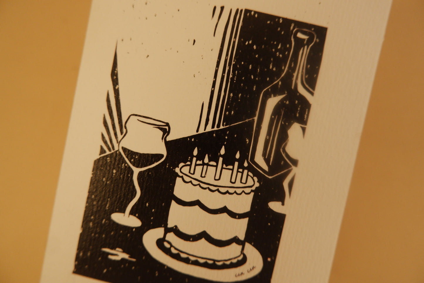 Black and white illustration of a cake with lit candles, wine glasses, and a bottle on a beige background.