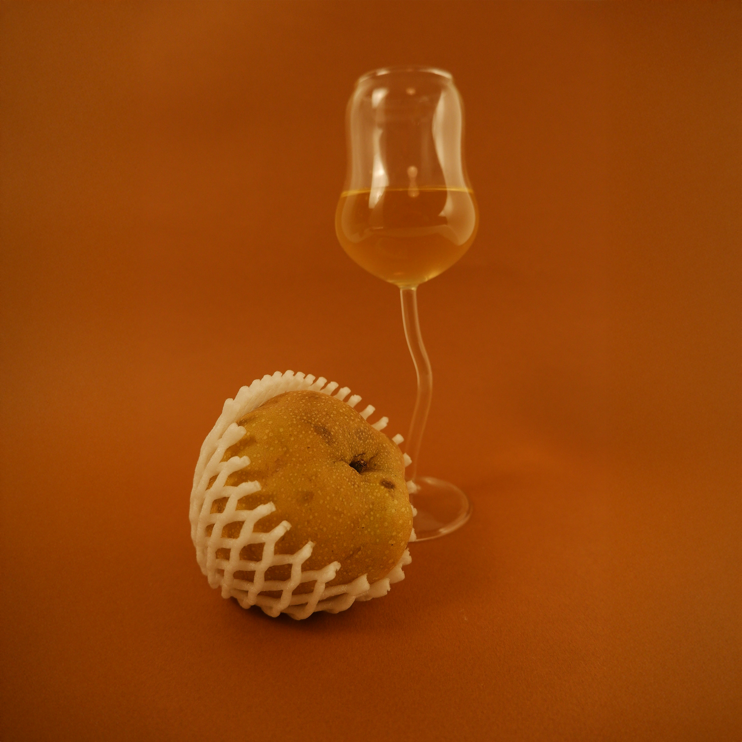 Fruit with a wine glass filled with a yellow liquid on an orange background