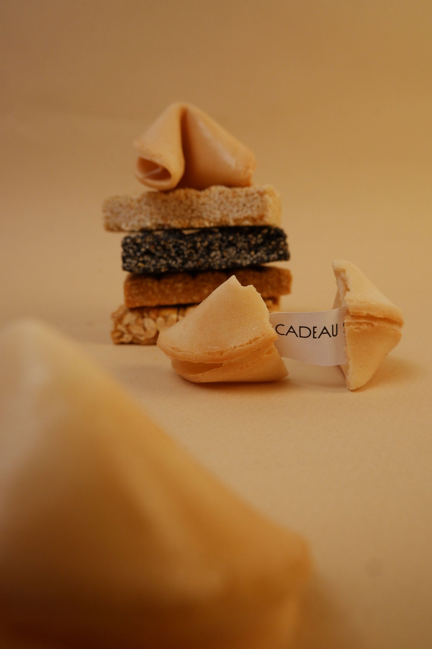 Stack of fortune cookies with a 'CADEAU' tag on a beige background