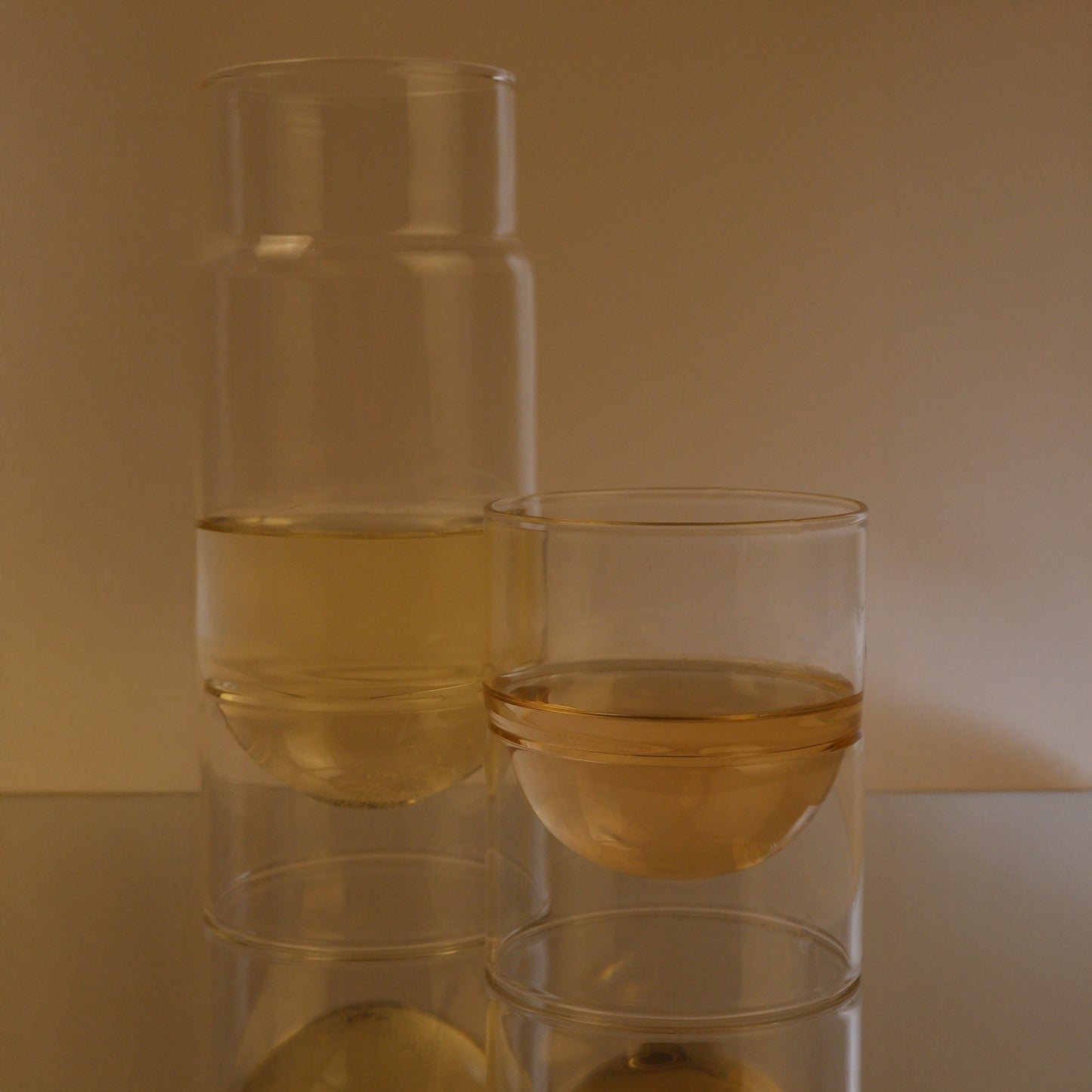 Two glasses of white wine stacked on a reflective surface with a neutral background