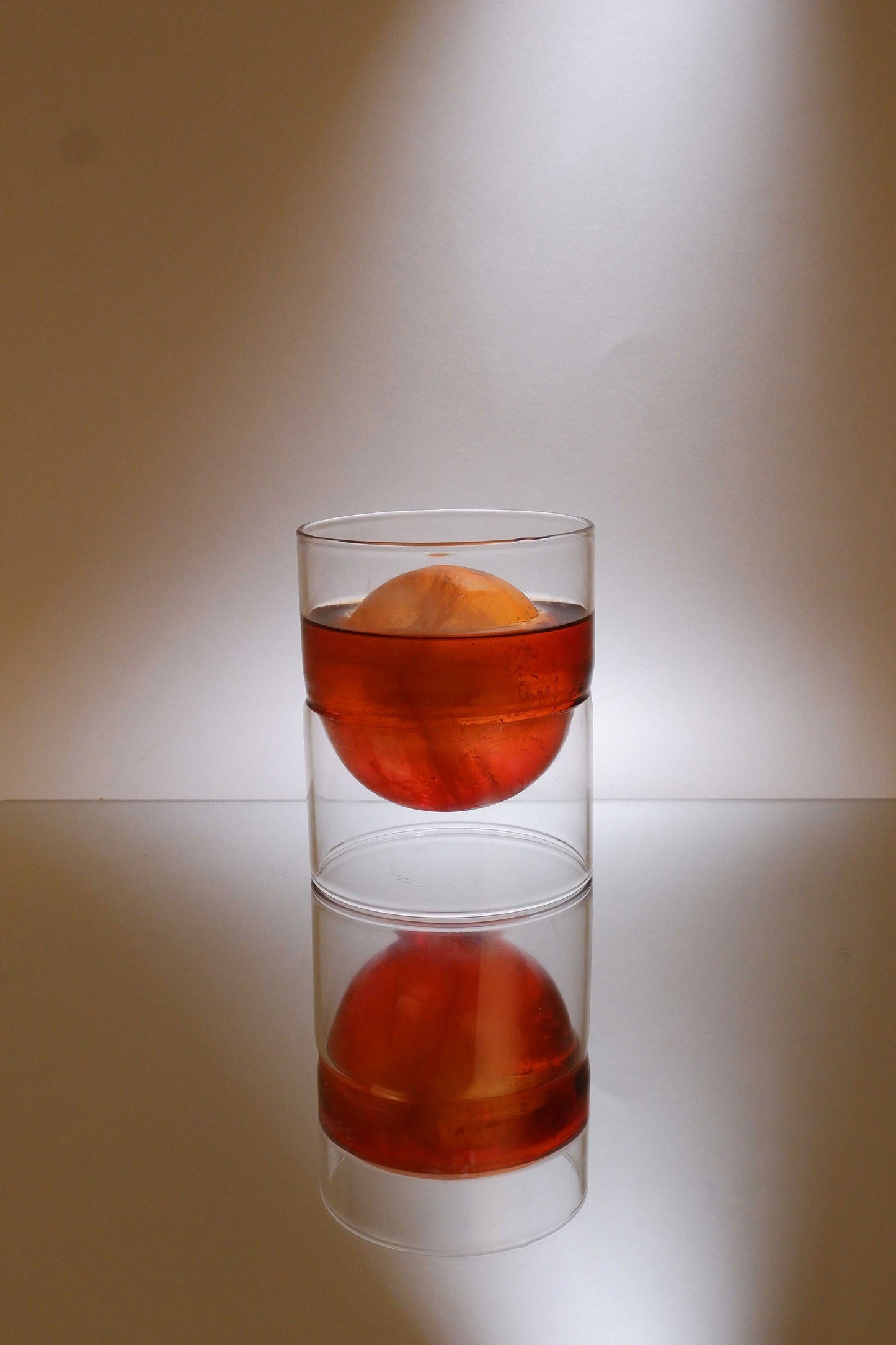 Clear glass with a red liquid and an orange slice on a reflective surface.