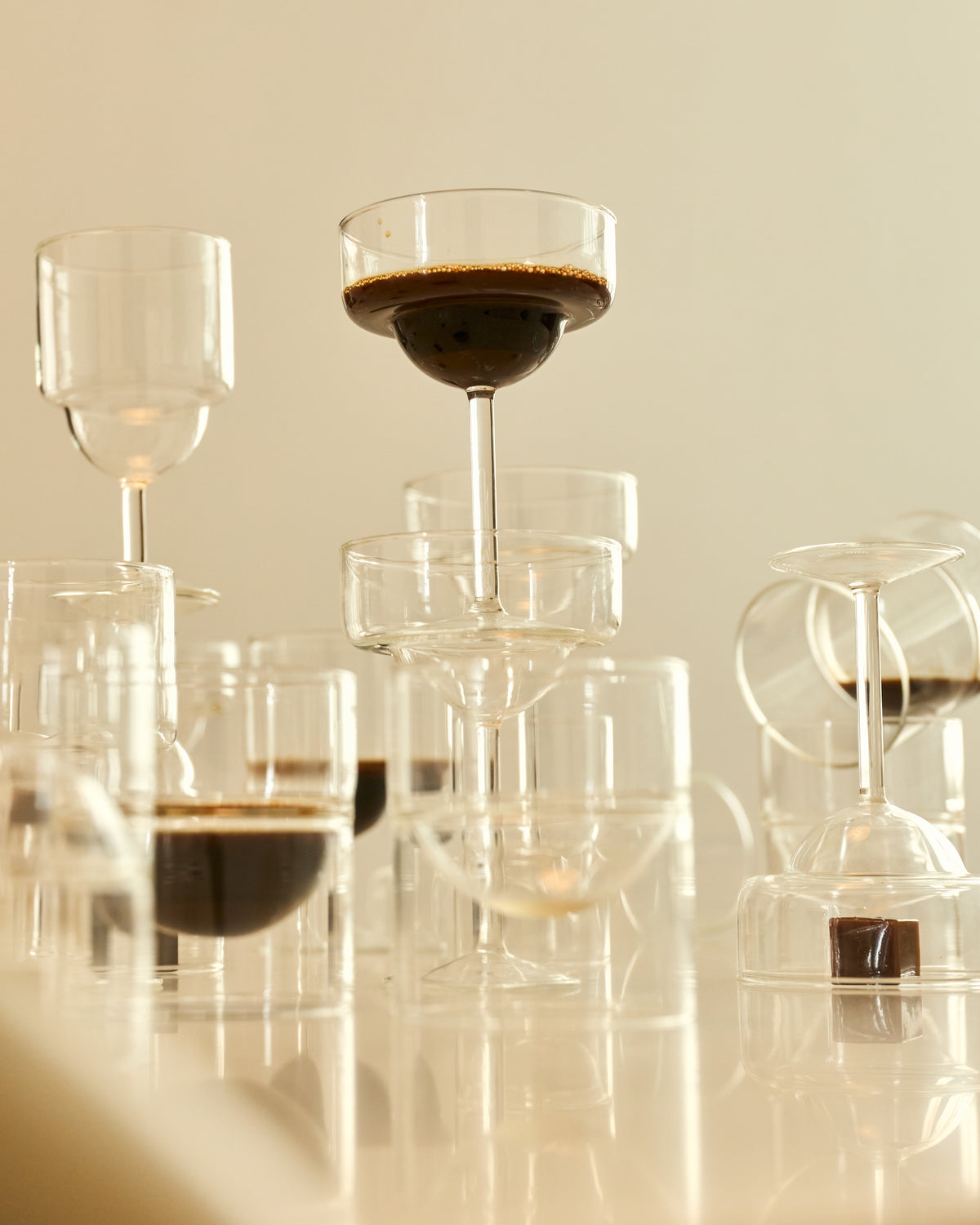 Stacked clear glass tumblers with coffee on a reflective surface