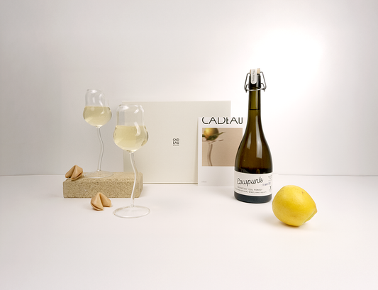 Bottle of white wine, two glasses with wine, a lemon, and a magazine on a white surface.