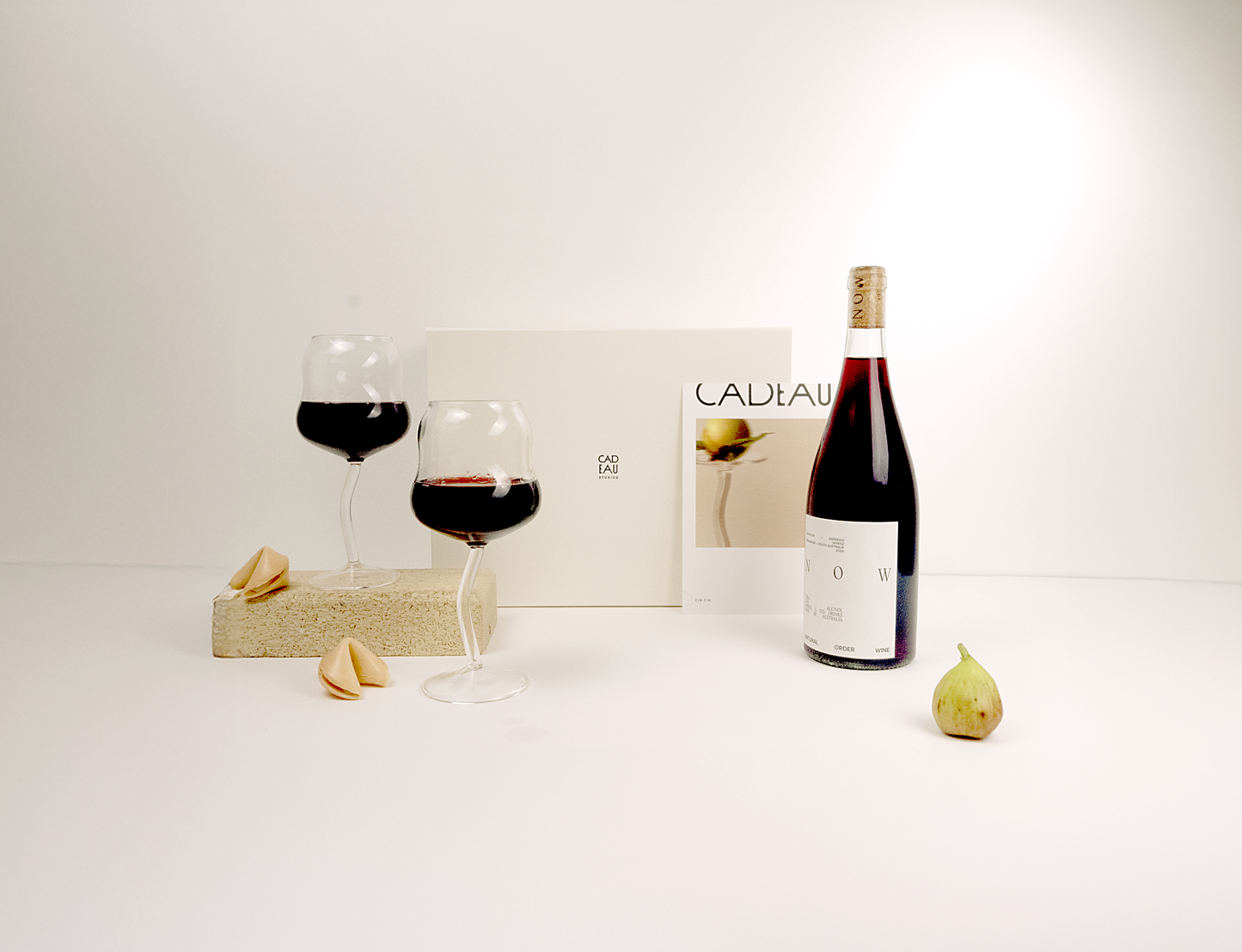 Wine bottle, glasses, and figs on a white surface with a magazine in the background.