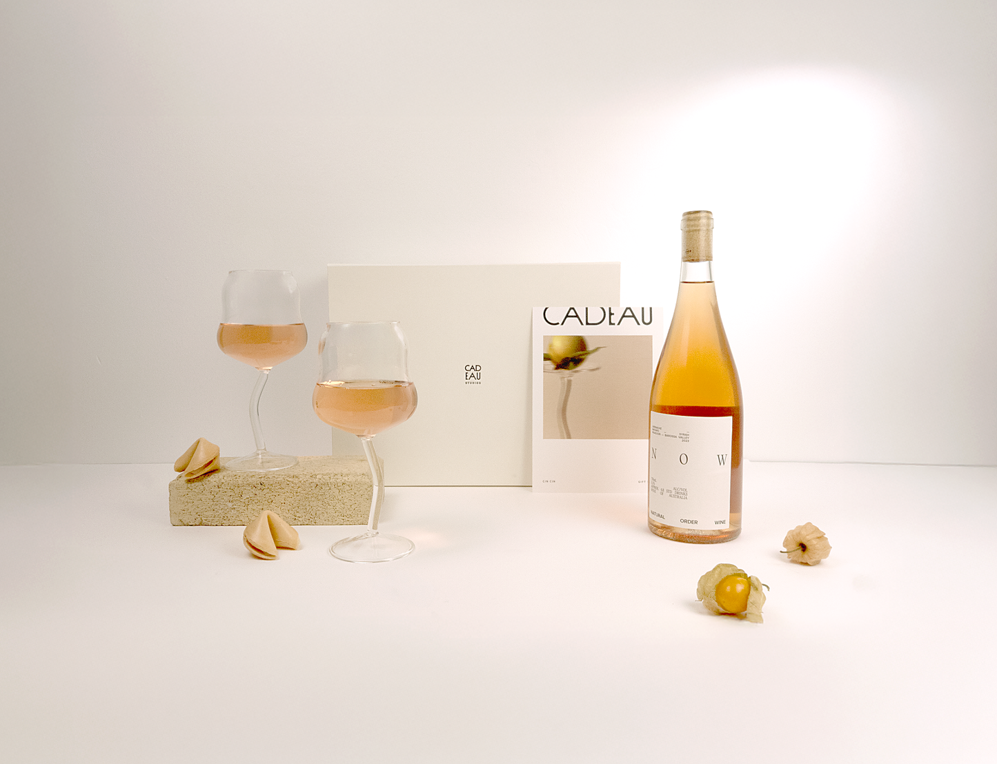 Bottle of Cadeau wine with two glasses and a magazine on a white surface
