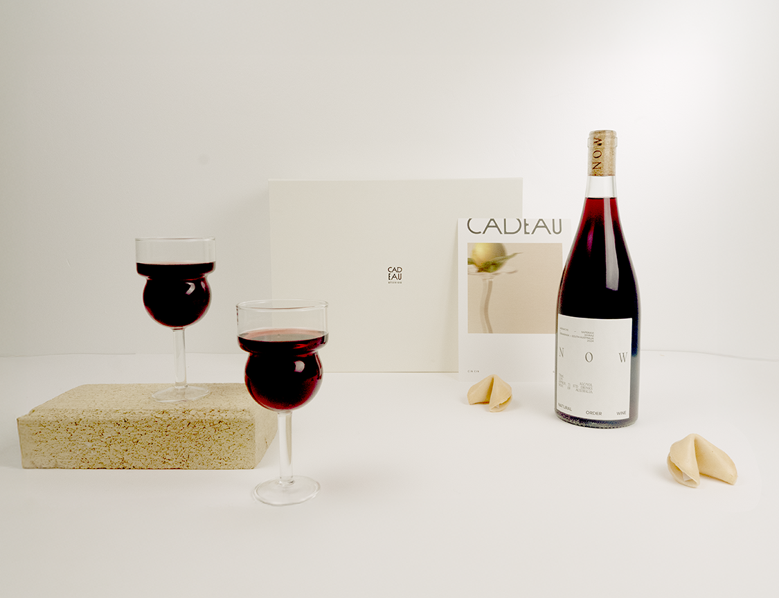 Bottle of red wine with two glasses and a magazine on a white surface