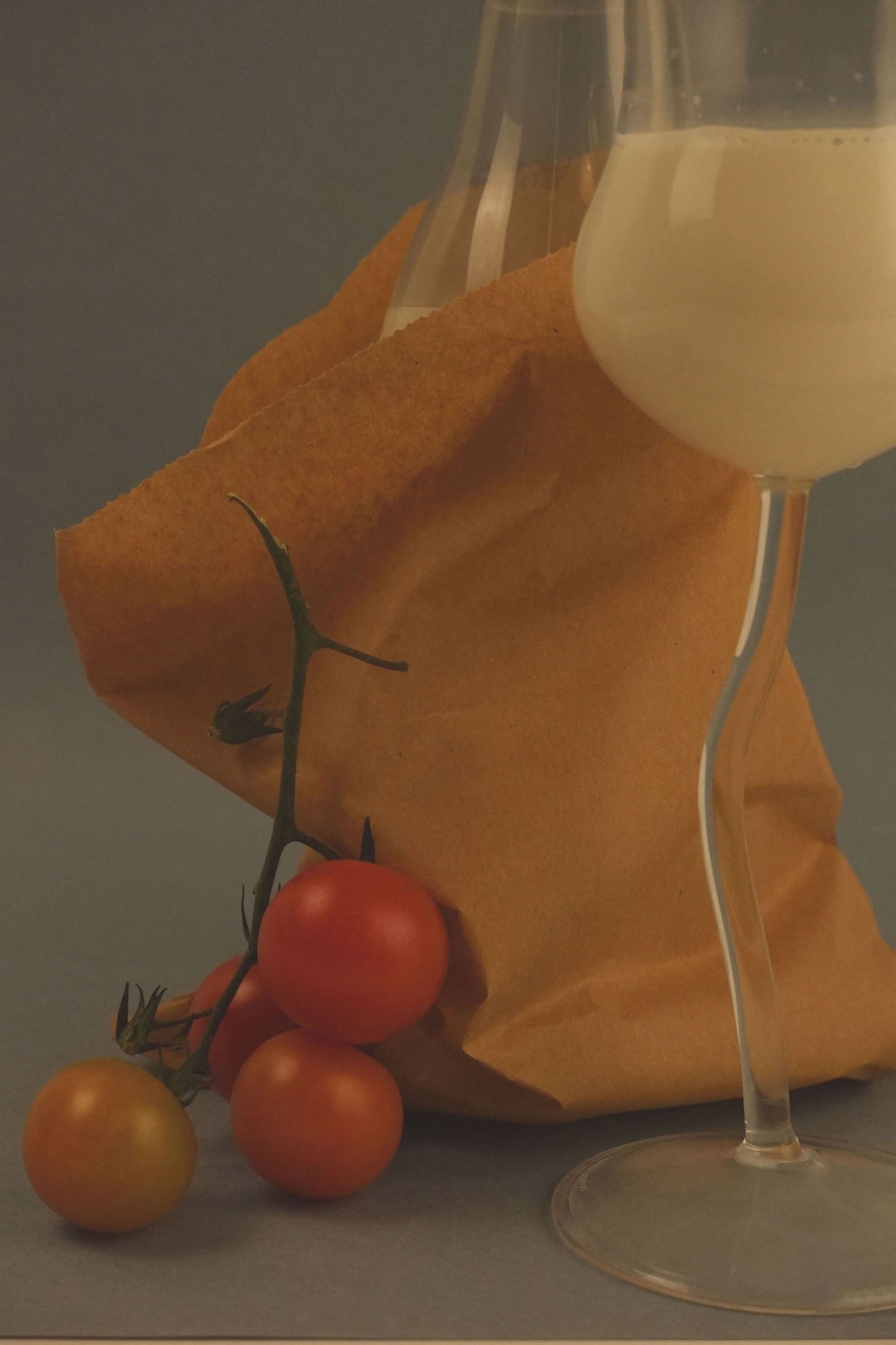 Wine glass with a drink, tomatoes, and a paper bag on a gray surface