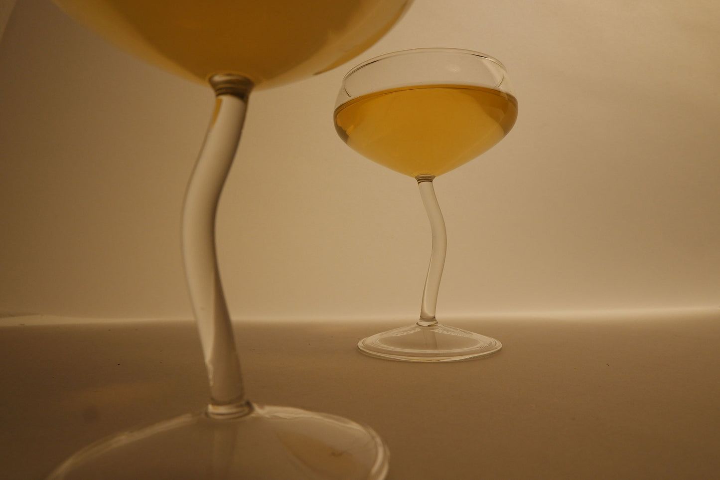 Two glasses, one filled with a yellow liquid, on a neutral background.