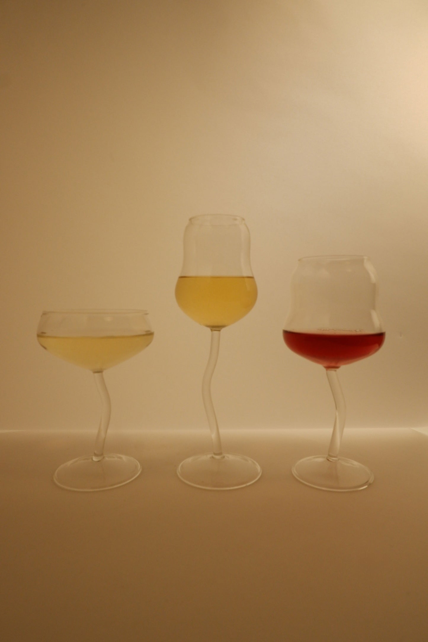 Three wine glasses filled with different colored liquids on a plain background