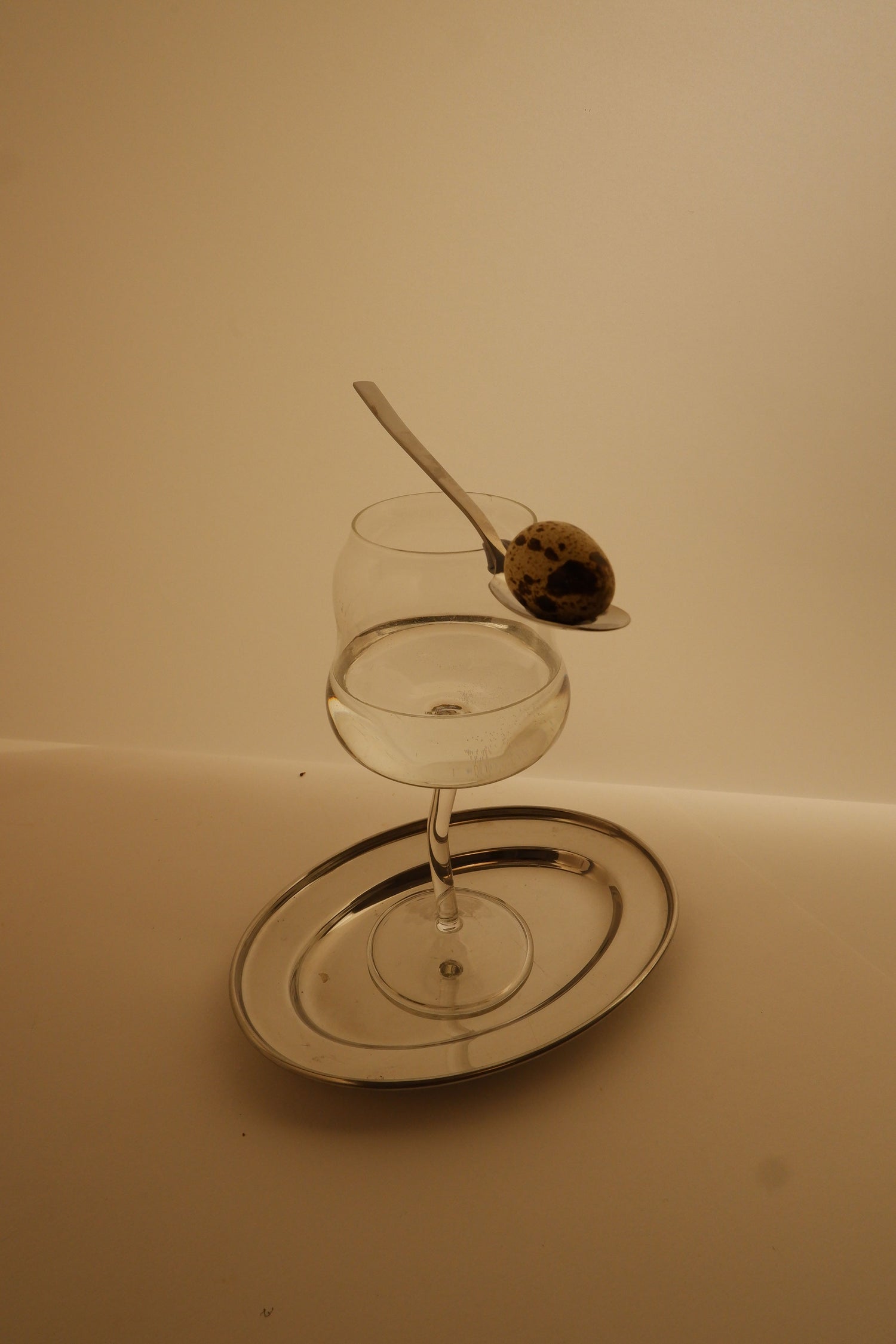 Clear cin cin wine glass with a spoon and olive on a white plate against a beige background