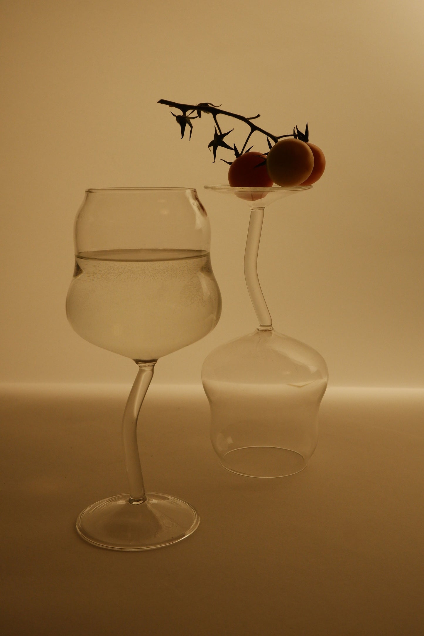 Two glasses, one filled with water and the other empty, on a plain background.
