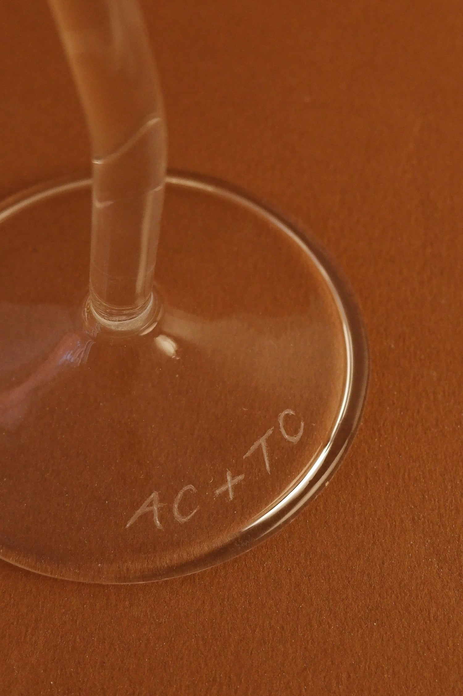 Close-up of a glass with 'AC+TC' engraving on a brown background