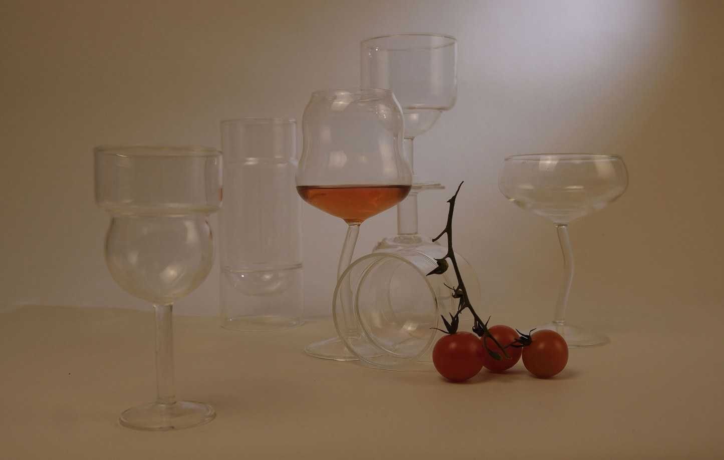 Set of empty and partially filled cin cin glassware with cherry tomatoes on a neutral background