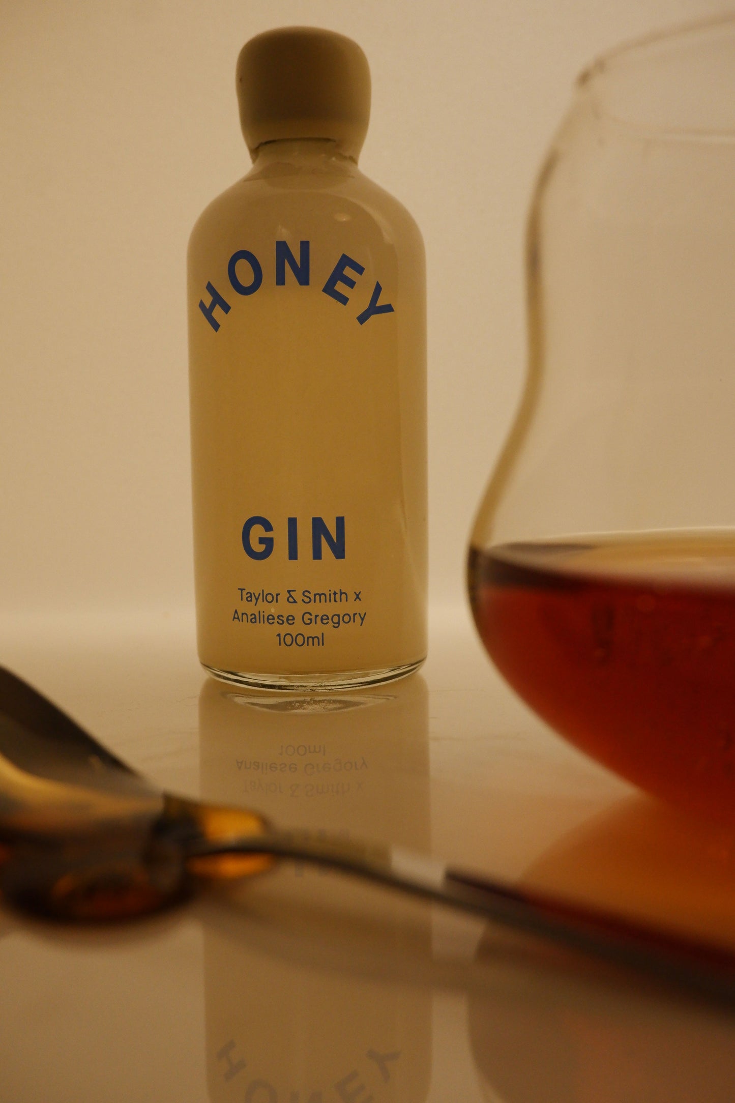 Bottle of Honey Gin with a glass of gin and honey on a reflective surface.