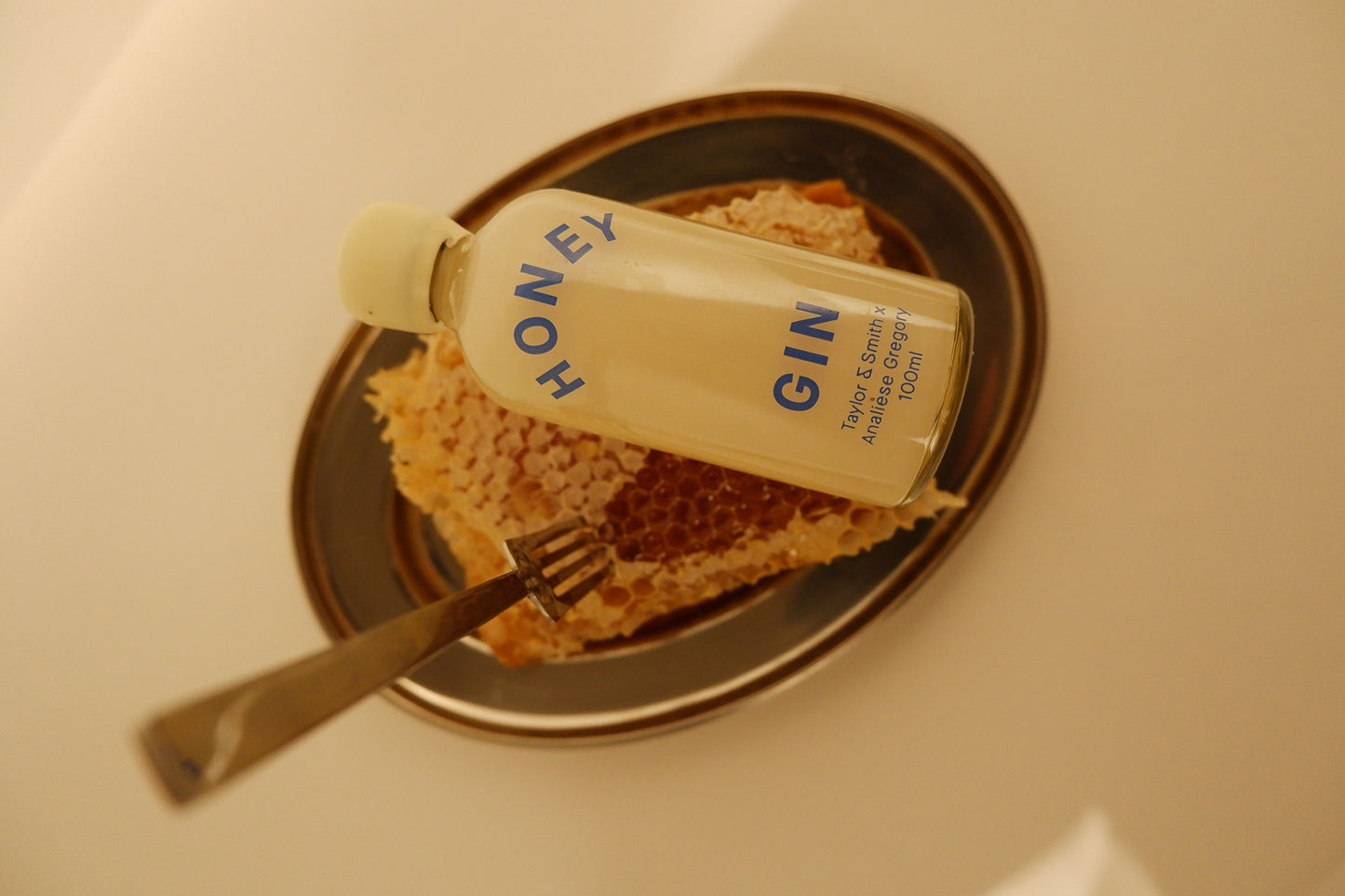 Bottle of TONEL Gin on a plate with honeycomb and a fork, inside a sink.