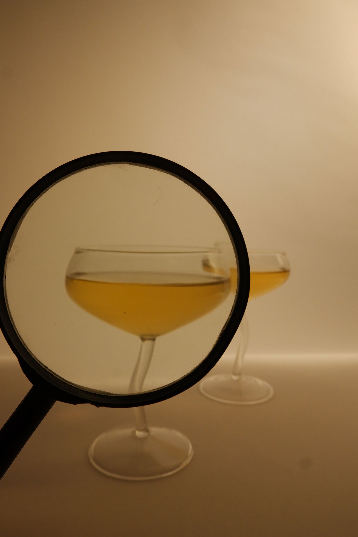 Glass of yellow liquid through a magnifying glass on a beige background