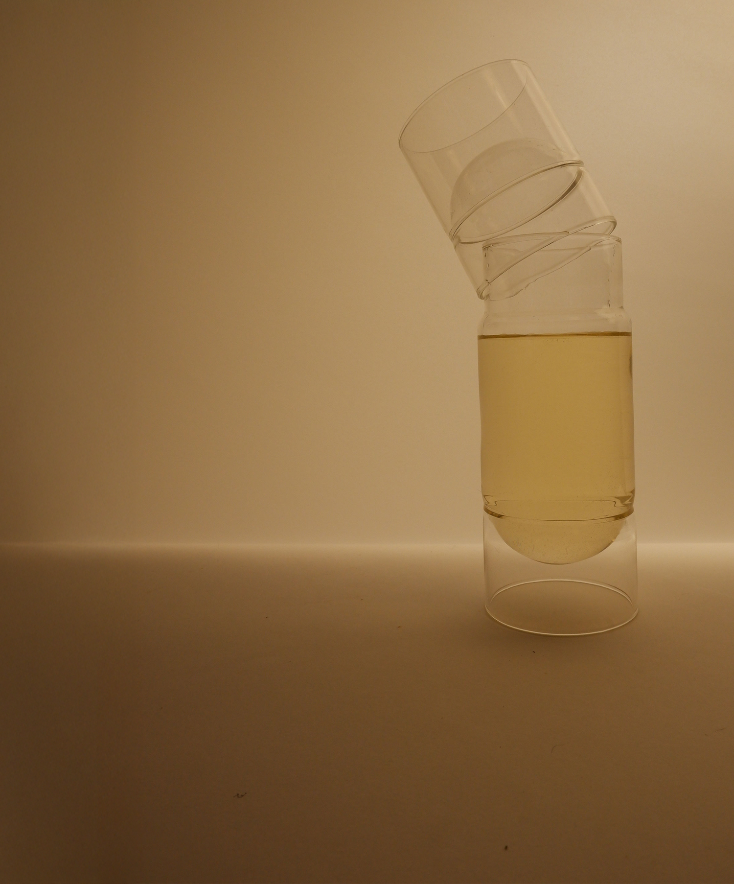 Two stacked glass containers with a yellow liquid on a beige background