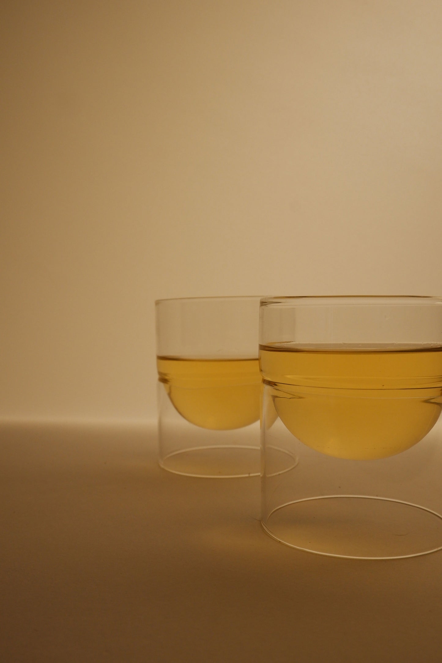 Two glasses filled with a yellow liquid on a beige background