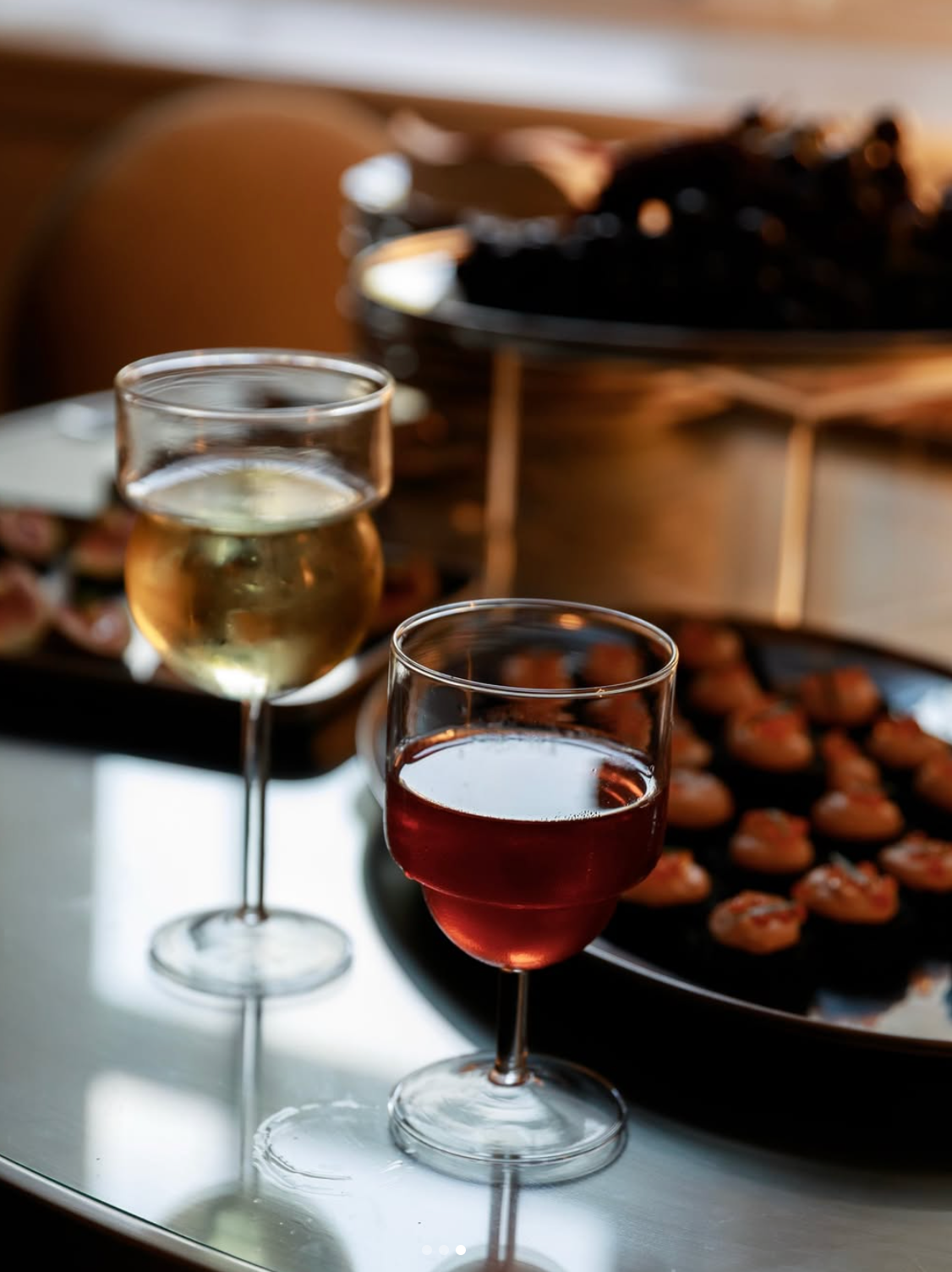 Two glasses of wine on a table with appetizers in the background