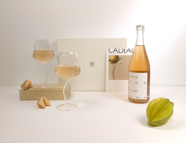 Bottle of Cadeau sparkling wine with two glasses and a star fruit on a white surface. - Rosé