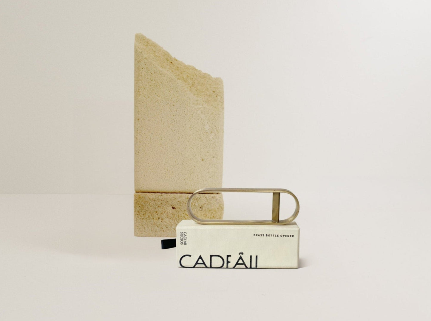 brass bottle opener on a light beige background with 'Cadeau' branding.