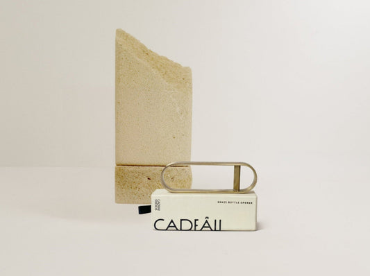 brass bottle opener on a light beige background with 'Cadeau' branding.